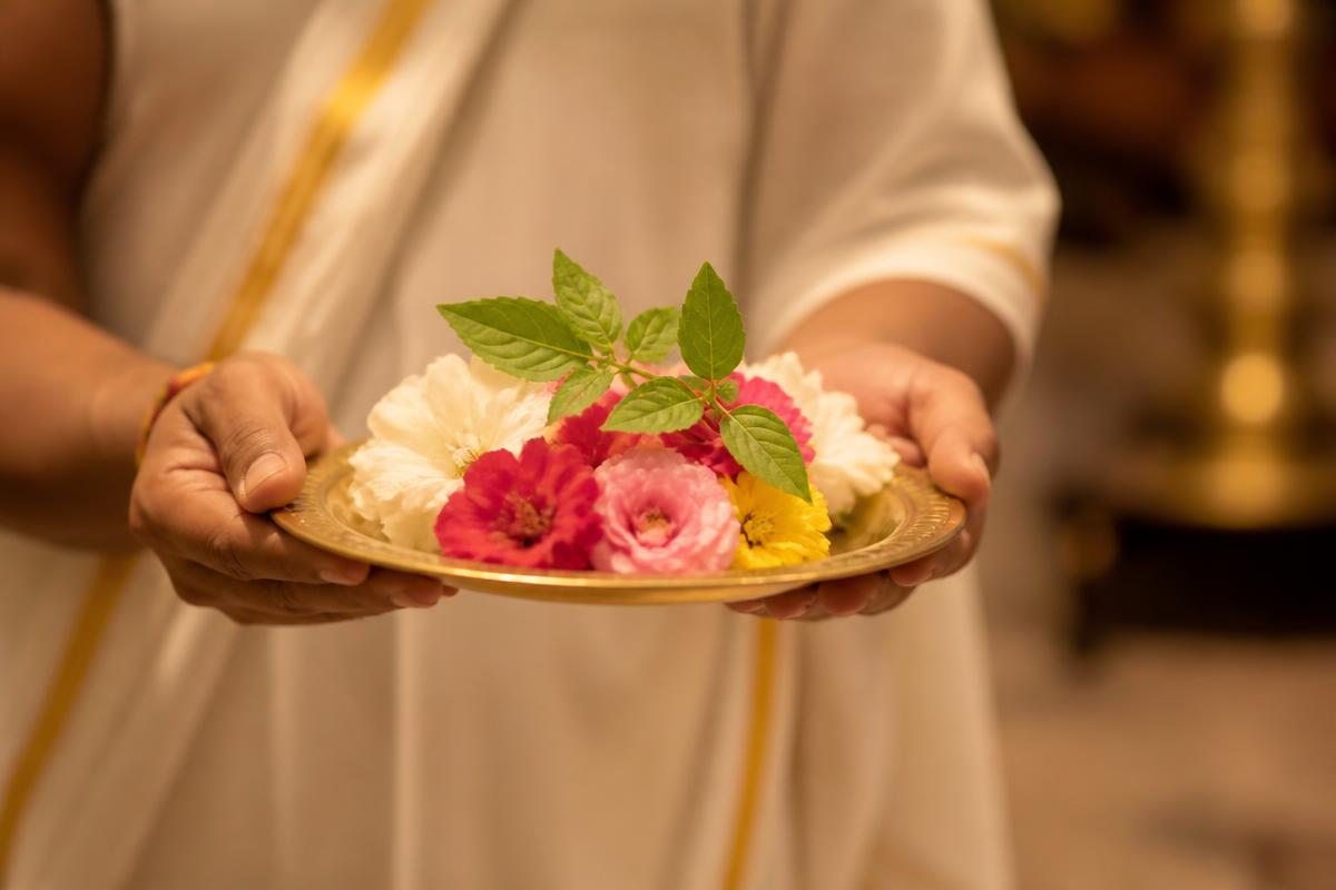 A servitor offering flowers and tulsi on a brass plate